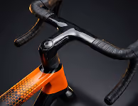 Close-up of orange and black bicycle handlebars with textured grip tape on a dark background.