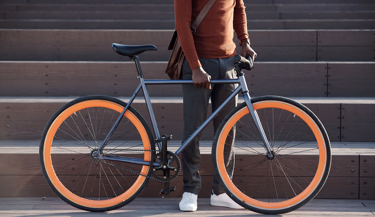 Person holding gray bike with bright orange wheels standing in front of wooden steps.