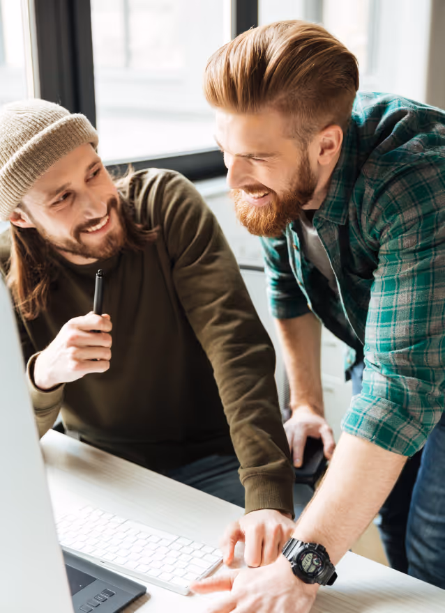 Two men smiling and collaborating while looking at a computer screen in a bright office.