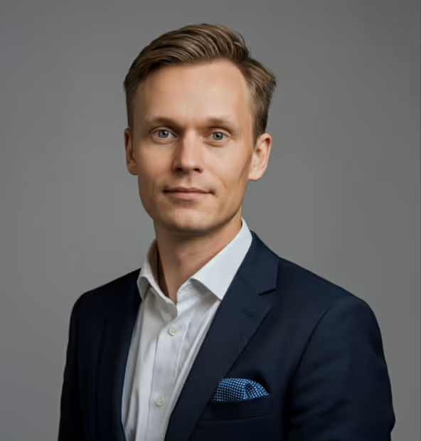 Professional headshot of a man with light brown hair wearing a navy suit jacket, white shirt, and blue patterned pocket square against a gray background.
