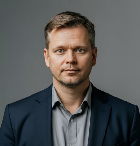 Man with short light brown hair wearing a blue blazer and light gray shirt against a gray background.