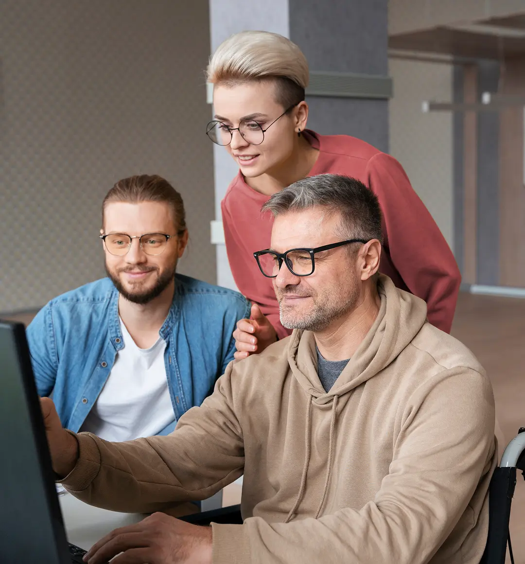 Three young professionals wearing glasses collaboratively working on a desktop computer in an office.
