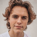 Young person with wavy brown hair and light skin, looking at the camera with a neutral expression.